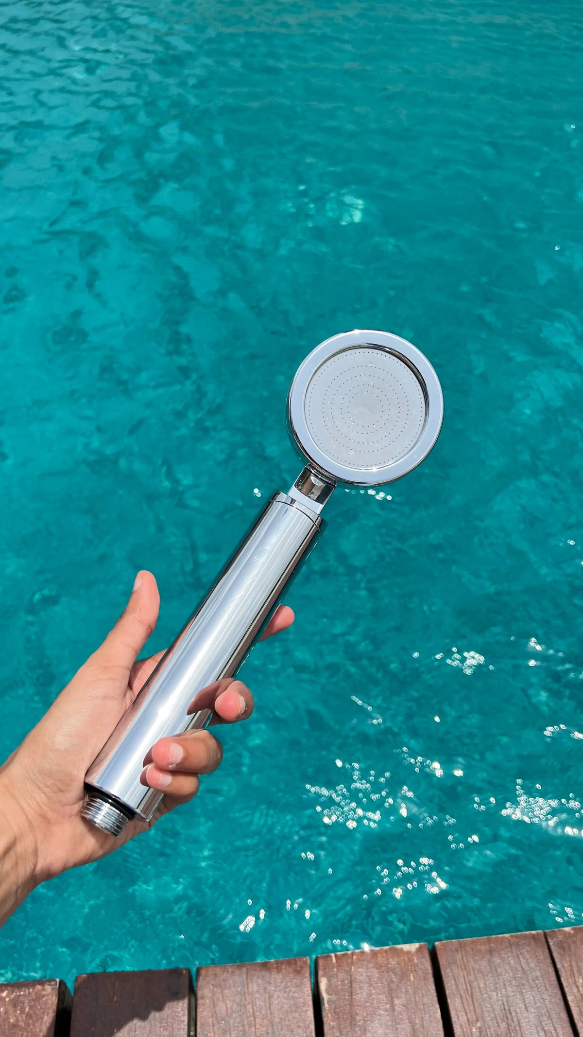 Hand holding a Luscentra handheld shower filter over a swimming pool.