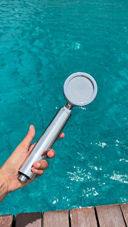 Hand holding a Luscentra handheld shower filter over a swimming pool.