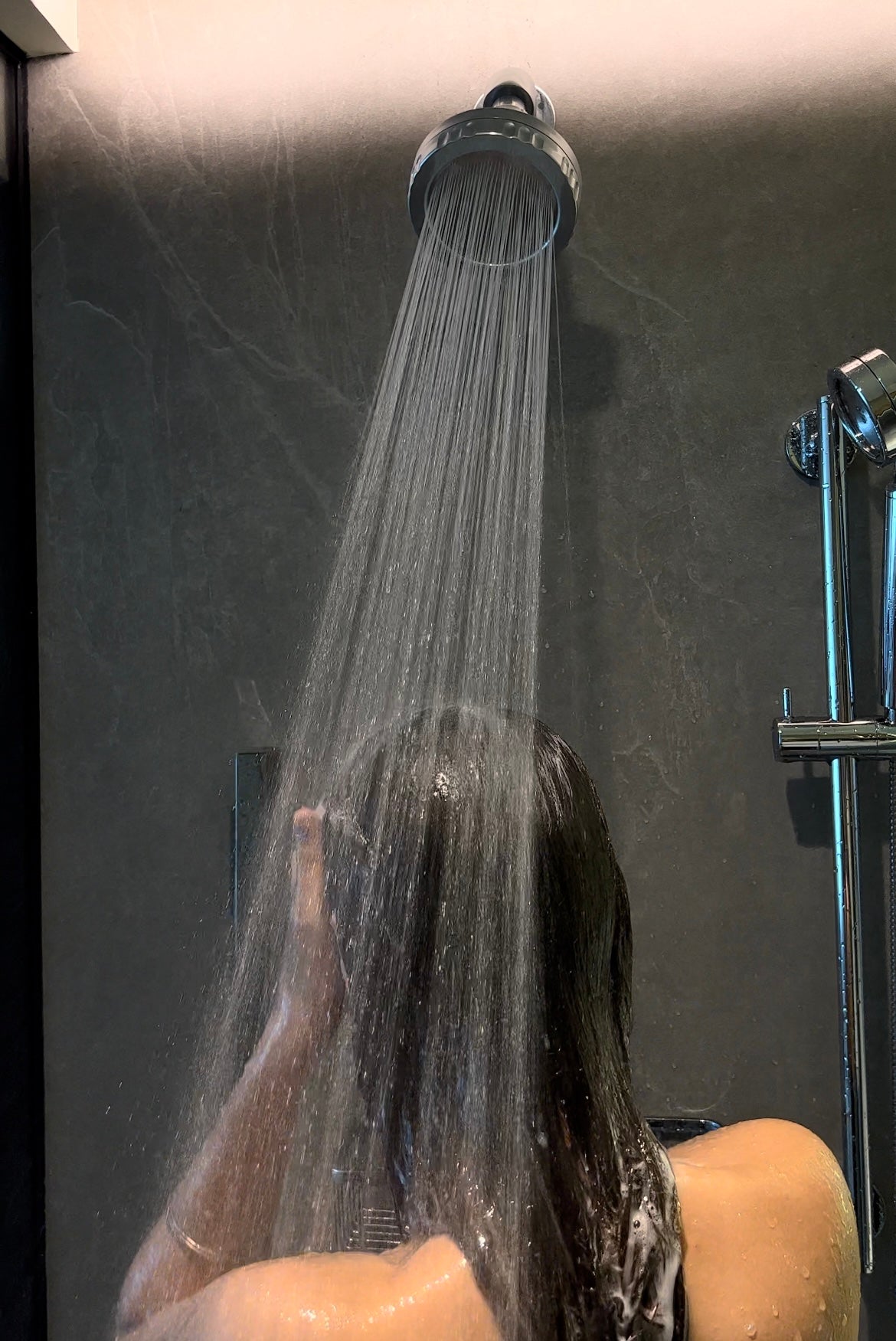 Person rinsing wet hair with a Luscentra handheld shower filter.