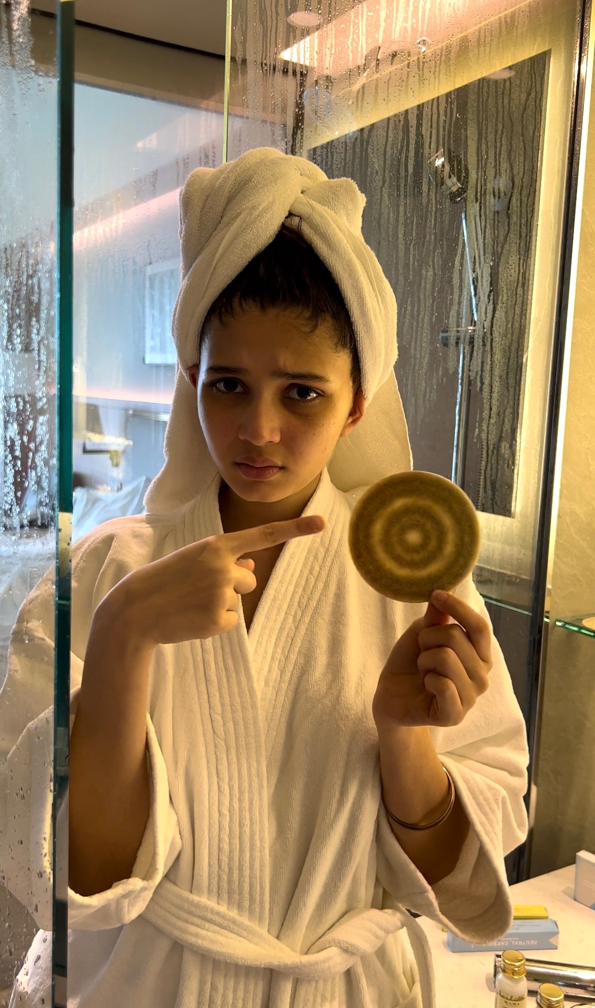 Woman in a bathrobe holding a used round microfibre shower-filter cloth.